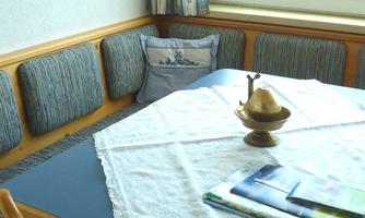 A cozy dining area with a blue tablecloth and a table runner. On the table are some magazines and a decorative pitcher.