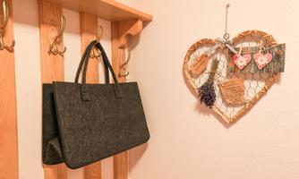 A gray bag hangs on a wooden wall with hooks. Next to it is a heart-shaped wall hanger with decorative elements and notes.