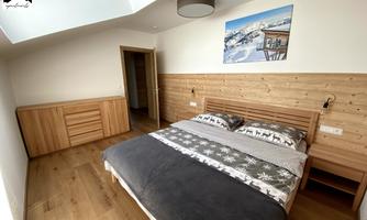 A bright bedroom with a large bed and wooden details. A picture of a mountain landscape hangs on the wall.