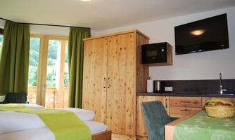 A cozy room with two beds, a television, and wooden cabinets. Large windows offer a beautiful view of nature.