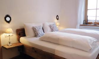 A cozy bedroom with two single beds and soft lighting. The walls are light and there is a window that lets in daylight.