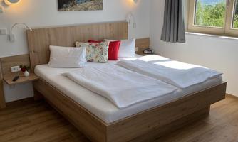 A modern bedroom with a large bed and wooden furniture. The window offers a beautiful view of the mountains.