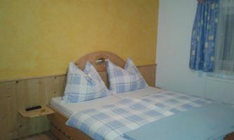 A cozy bedroom with a wooden bed and dotted pillows. The walls are painted in warm yellow tones and there is a window with blue curtains.