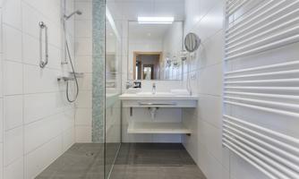 A modern bathroom with a glass shower and a white sink. The walls are tiled with light tiles and a towel radiator is visible.