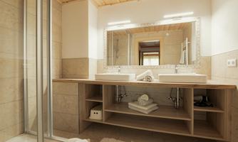 A modern bathroom with two sinks and a large mirror. The decor is bright and simple with wood and stone surfaces.