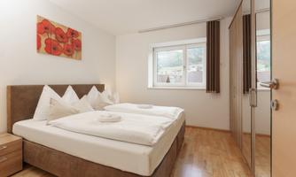 A cozy bedroom with two single beds and white bedding. The room has large windows and natural wooden floors.