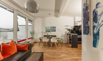 A modern apartment with wooden floors and large windows.  
The dining area is bright and inviting, with a stylish table and colorful chairs.