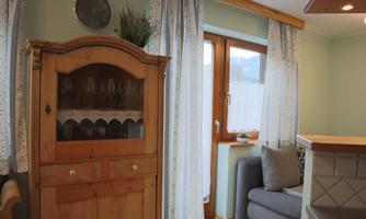 A cozy living space with a wooden cabinet and a gray sofa. The windows are adorned with curtains and let in plenty of light.