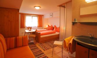 A cozy room with wooden decor, two beds, and a small table. The room is bright and friendly with orange furnishings.