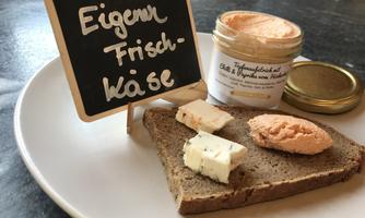 A piece of bread with two different types of cheese and a glass of cream cheese. Next to it is a small sign that reads "Own Cream Cheese."