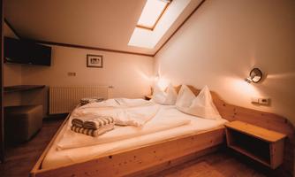 A cozy bedroom with a double bed and wood paneling. The room has a window and modern amenities like a television.