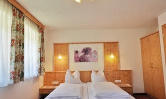 A cozy bedroom with two beds and light wood decor. Large windows provide plenty of daylight and a friendly atmosphere.