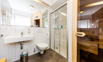 A modern bathroom with a shower cubicle and a washbasin. The walls are tiled in light colors and there is a sauna in the corner.