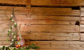 A rustic wooden wall with engraved names and patterns. In the foreground, there is a decorative arrangement with a wire tree, apples, and flowers.