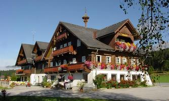 A traditional alpine wooden house with blooming balconies. Surrounded by a green meadow and clear mountain landscape.