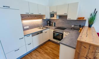 A modern kitchen with bright cabinets and a functional work surface. The floor is made of wood and there is pleasant lighting.