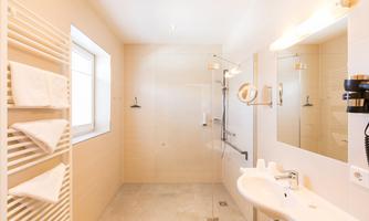 A modern bathroom with a shower, a sink, and a large mirror. White towels are neatly hung, and the walls are bright and inviting.
