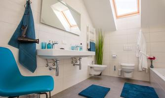 A modern bathroom with a sink, a mirror, and blue accents. The room is bright and has a skylight that provides natural light.