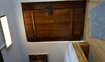 A rustic wooden door in an interior with a bed and a carpet. The walls are painted light, and there is a picture on the wall.