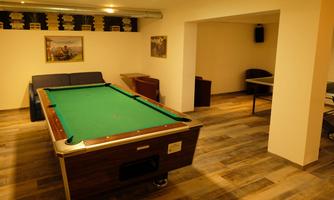 A cozy room with a billiard table and a seating area. The walls are light, and the floor has a wood look.