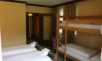A simple room with a bunk bed and two single beds. The walls are in soft colors and the room has windows with curtains.