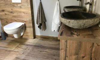 A modern bathroom with wooden walls and a wooden washbasin. Two round stone sinks are placed next to a toilet bowl.