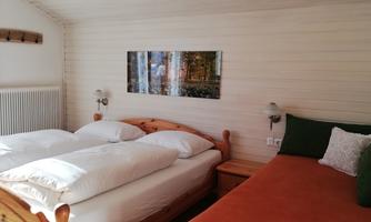 A cozy bedroom with two beds and an additional sofa. A picture of a forest hangs on the wall.
