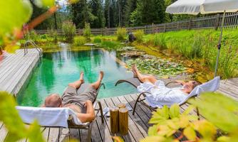 A relaxing area by the pond with two people in lounge chairs. Surrounded by lush greenery and a tranquil atmosphere.