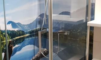 A modern shower with a glass partition and a landscape motif on the back wall. The view shows a calm lake and mountains in the background.