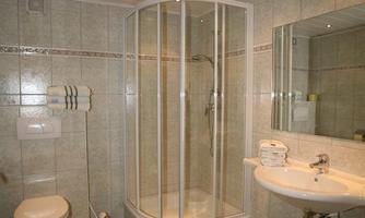 A modern bathroom with a shower cubicle and a sink. The walls are decorated with light tiles, and there are yellow bath mats.