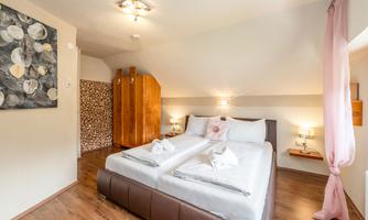 A modern bedroom with a large double bed and light wooden flooring. The walls are kept neutral, and there is a cozy atmosphere with soft lighting.