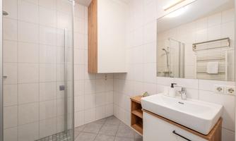 A modern bathroom with a shower and sink. Bright tiles and wood details create a pleasant atmosphere.