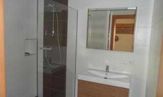 A modern bathroom with a glass shower and a sink. There is a mirror on the wall and some shelves.
