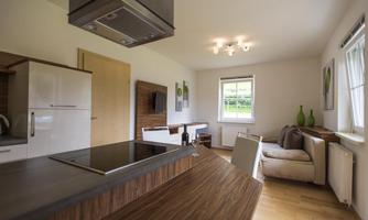 A modern kitchen with wooden surfaces and white cabinets. The space is bright and friendly, with a cozy seating area.