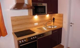 A modern kitchen with dark cabinets and a wooden countertop. It is equipped with a stove, an oven, and a sink.