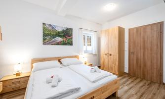 A cozy bedroom with a double bed and wooden furniture. A large window lets in plenty of light, and there is a beautiful picture on the wall.