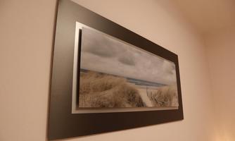 A beautiful wall picture featuring a landscape of sand dunes and a view of the sea under a cloudy sky. The soft colors give the room a calm atmosphere.