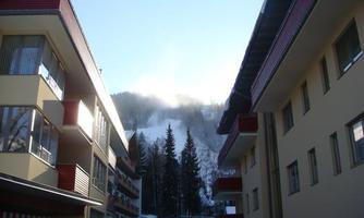 A view between residential buildings of snow-covered mountains. The sky is clear and there are light misty wisps.