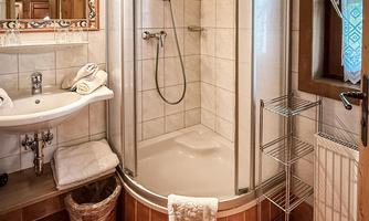 A modern bathroom with a shower cabin and a sink. The walls are tiled and there is a large mirror as well as natural wooden details.