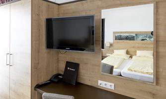 A modern room with a TV and a mirror. In the background, two beds and a desk can be seen.