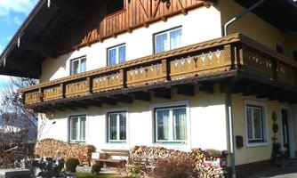A traditional alpine house with a wooden balcony. The garden is well-maintained and there are wood stacks next to the building.