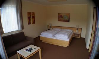 A cozy room with a double bed and a sofa. The walls are light, and there are some decorative pictures.
