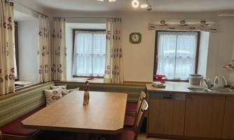 A cozy kitchen with a large table and comfortable chairs. The windows are decorated with curtains and the furnishings are modern.