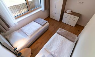 A bright room with two single beds and a window that lets in a lot of light. There is a modern furniture arrangement with a wardrobe and a table.