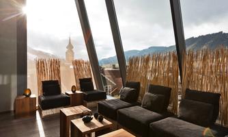 A modern living room with large windows and a view of the mountains. Dark furniture and wooden trays create a cozy atmosphere.