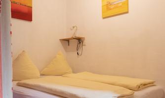 A simple bedroom with a double bed and two pillows. Two painted pictures are hanging on the wall.