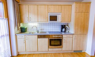 A modern kitchen with light wood cabinets and a simple design. It is equipped with a stove, a microwave, and a sink.