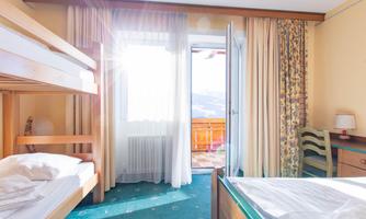 A bright room with a loft bed and a view of the balcony. The walls are painted in warm colors and the light streams through the curtains.