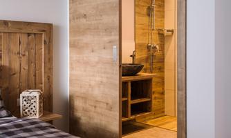 A modern bedroom with wooden details and a view of a bathroom. The bathroom features a shower and a stylish washbasin.