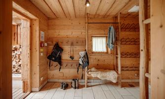 An inviting room made of wood with wall hooks for clothes and backpacks. The floor is tiled and there is a cozy seating area.